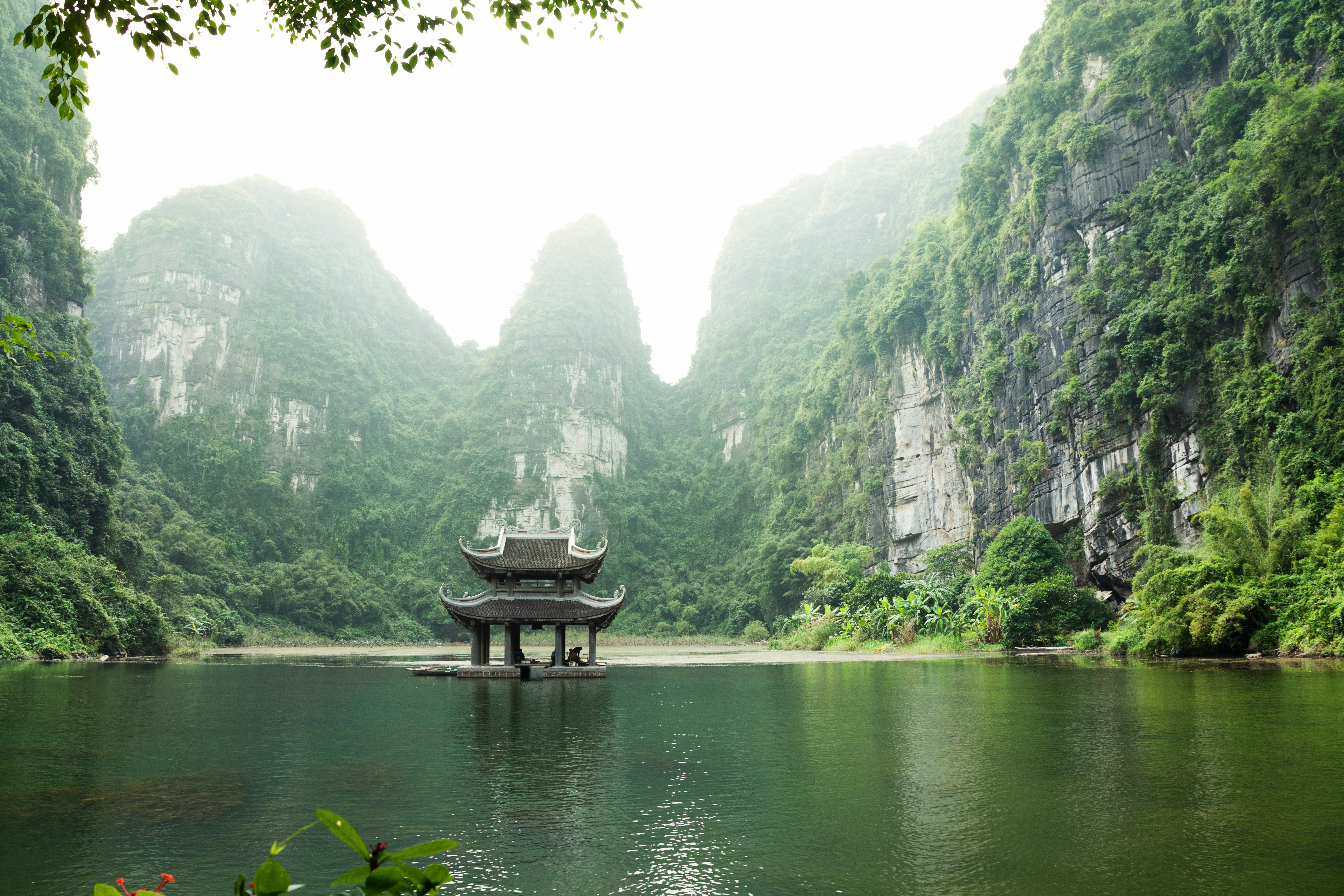 A pavilion on still water below karst cliffs