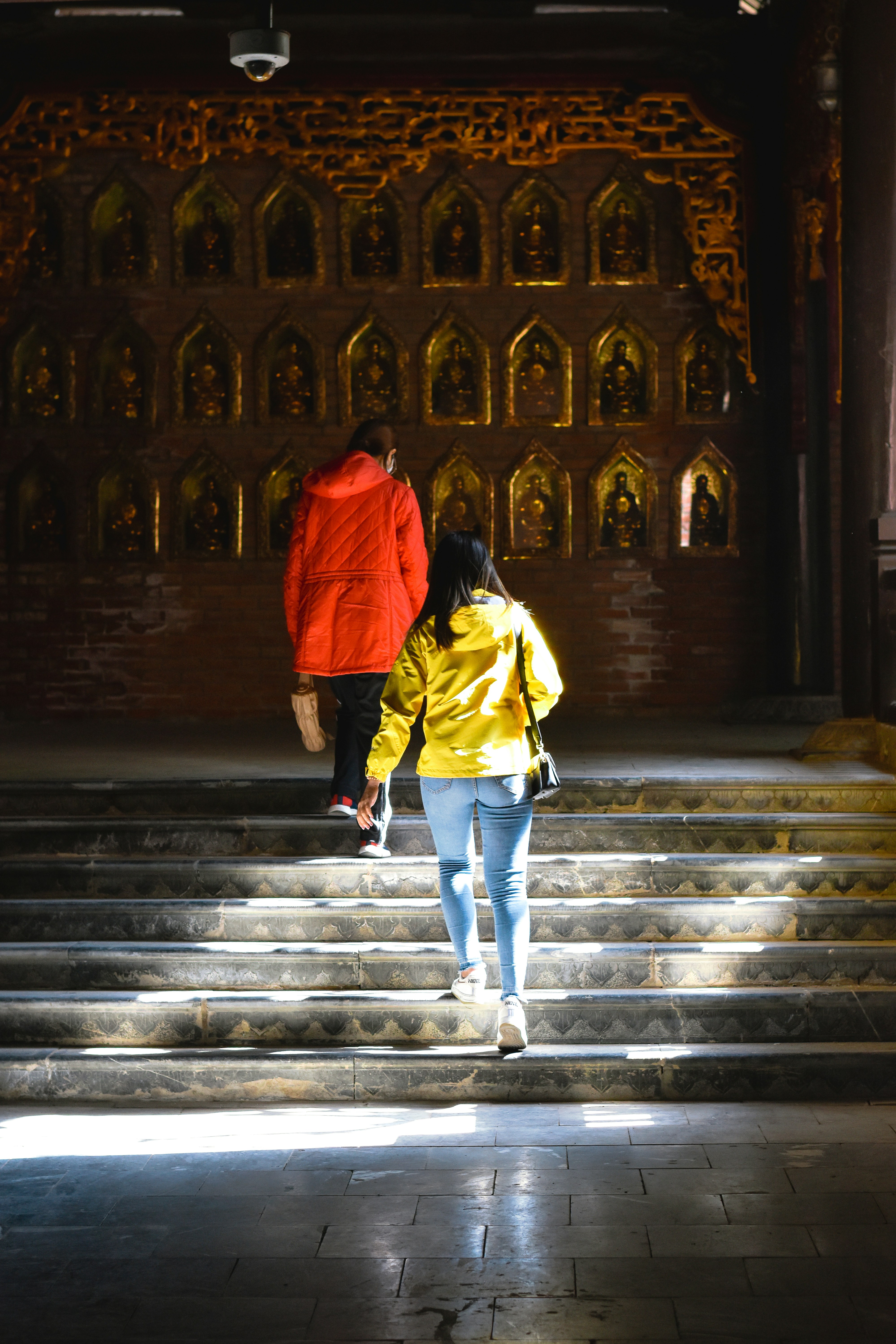 Visitors climbing temple steps past gilded Buddha niches
